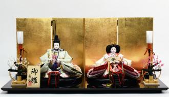黒塗の飾り台は、漆器の産地で有名な富山県の高岡塗で、屏風は金箔を貼って仕上げてあります。お人形は、京都西陣金襴に桜の刺繍のお衣裳で、春を先取りさせてくれるようなお祝いのイメージの親王飾りです。